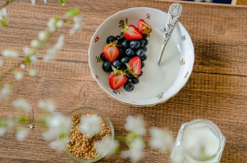 A bowl of fresh strawberries, blueberries with yogurt on a wooden table, viewed from above.
