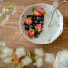 A bowl of fresh strawberries, blueberries with yogurt on a wooden table, viewed from above.